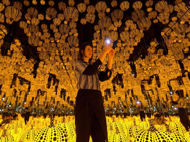 A gallery assistant poses for a photo with 'All the Eternal Love I Have for the Pumpkins' by Yayoi Kusama