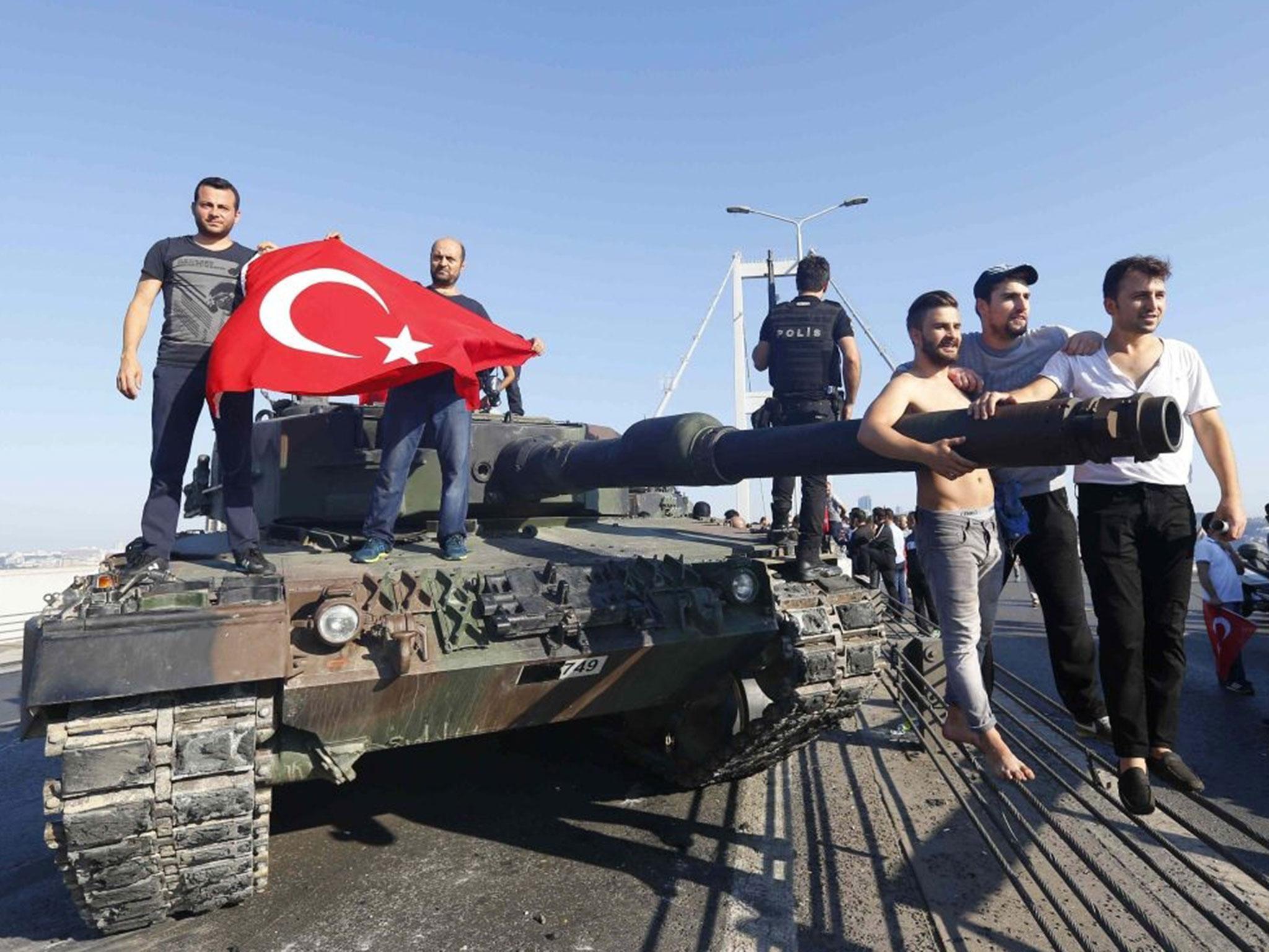 Civilians carry the Turkish flag onto a tank abandoned by rebel soldiers