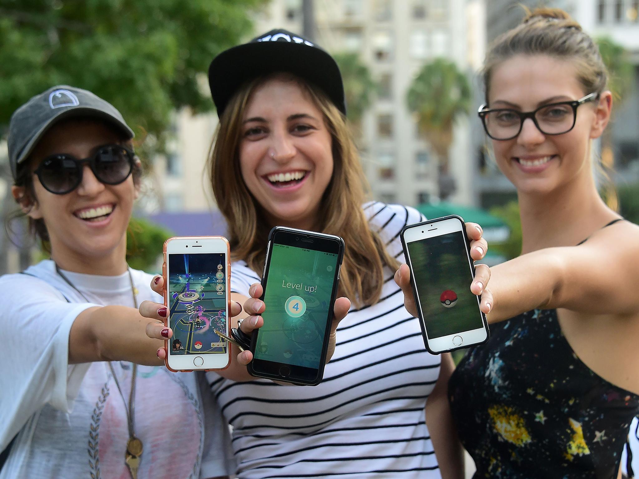 Three Pokemon Go enthusiasts display their cellphones while playing Pokemon Go on July 13, 2016 at Pershing Square in Los Angeles, California
