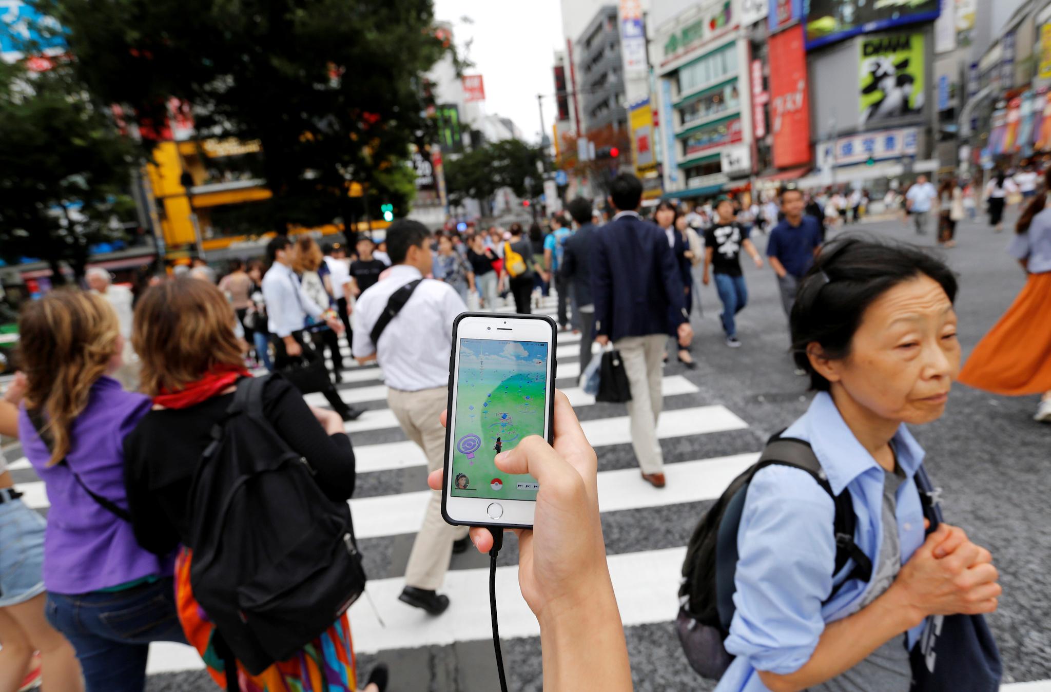 A man plays the augmented reality mobile game "Pokemon Go" by Nintendo on his mobile phone as he walks at a busy crossing in Shibuya district in Tokyo, Japan