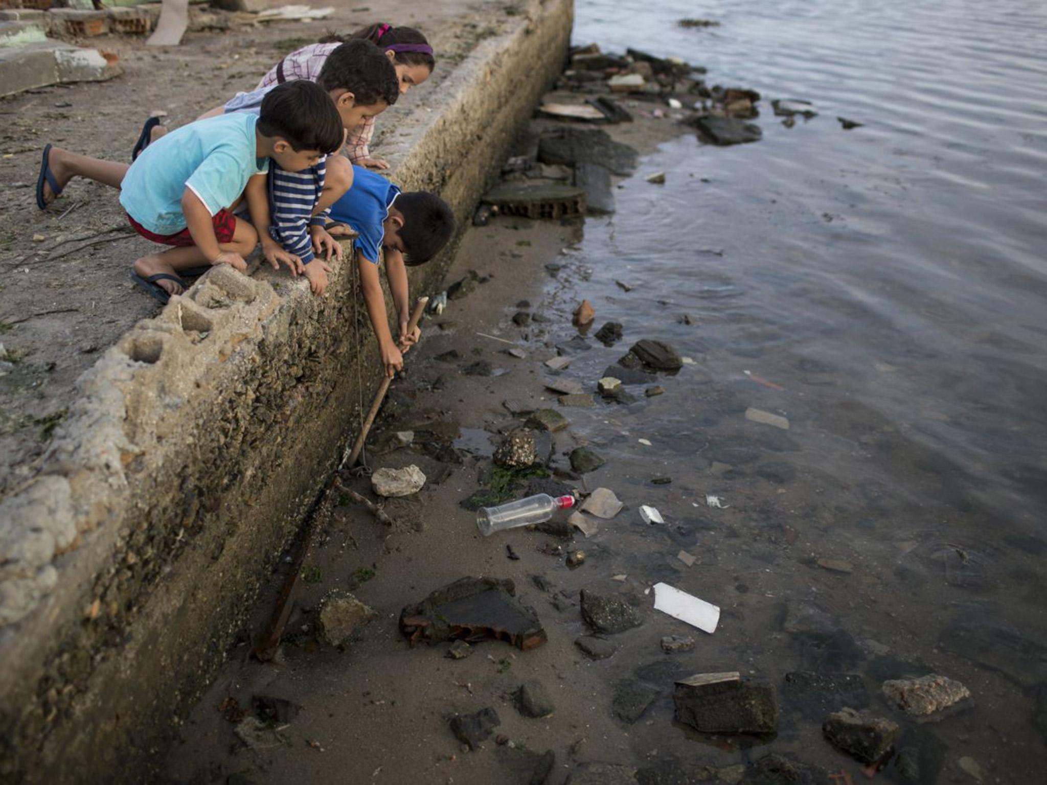 Children try to catch a crab as they play on the polluted shore of Guanabara Bay