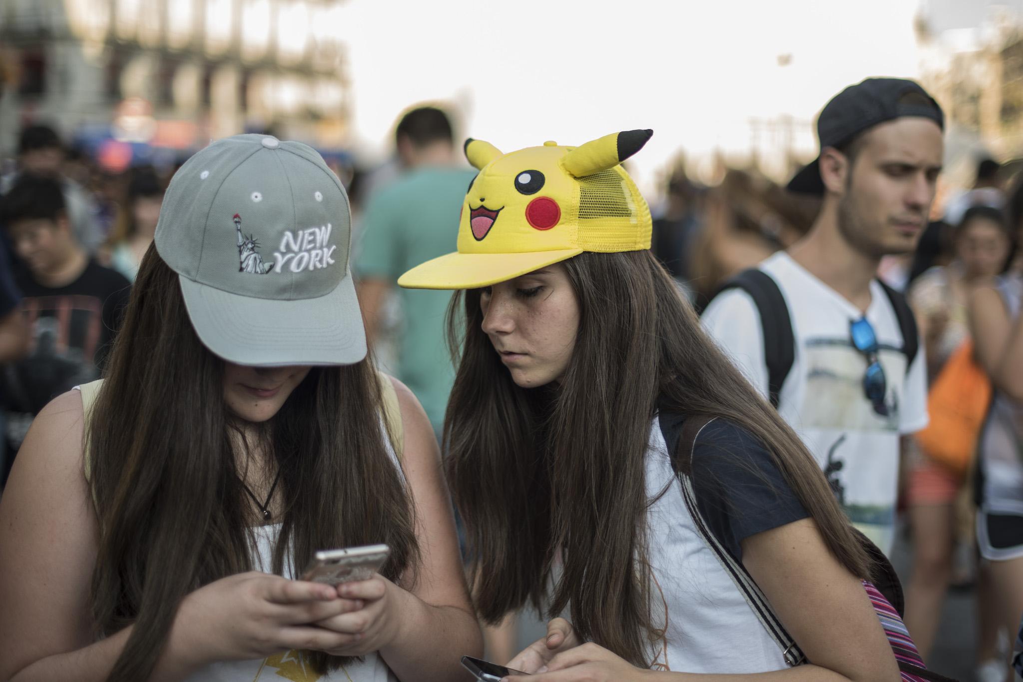 A girl sporting a 'Pikachu' hat looks at her friend as she uses the Pokemon Go application during a mass gathering in Madrid on July 28, 2016