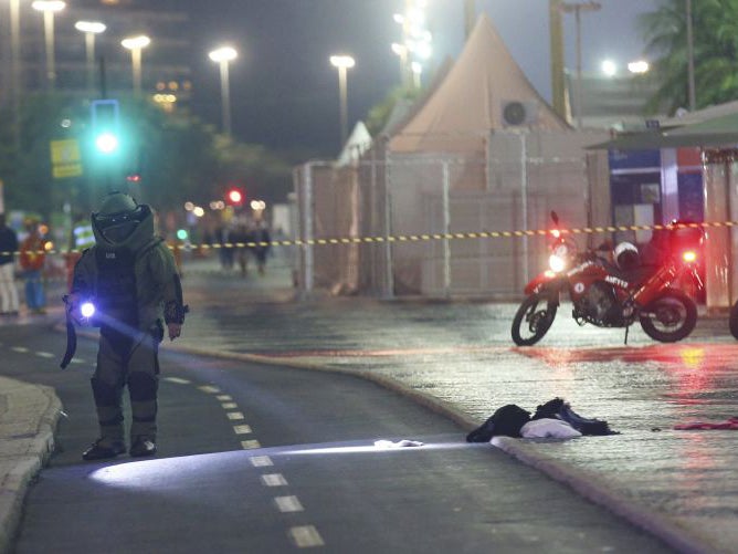 A bomb disposal expert wearing protective equipment examines a suspect package next to the beach volleyball arena during the opening ceremony