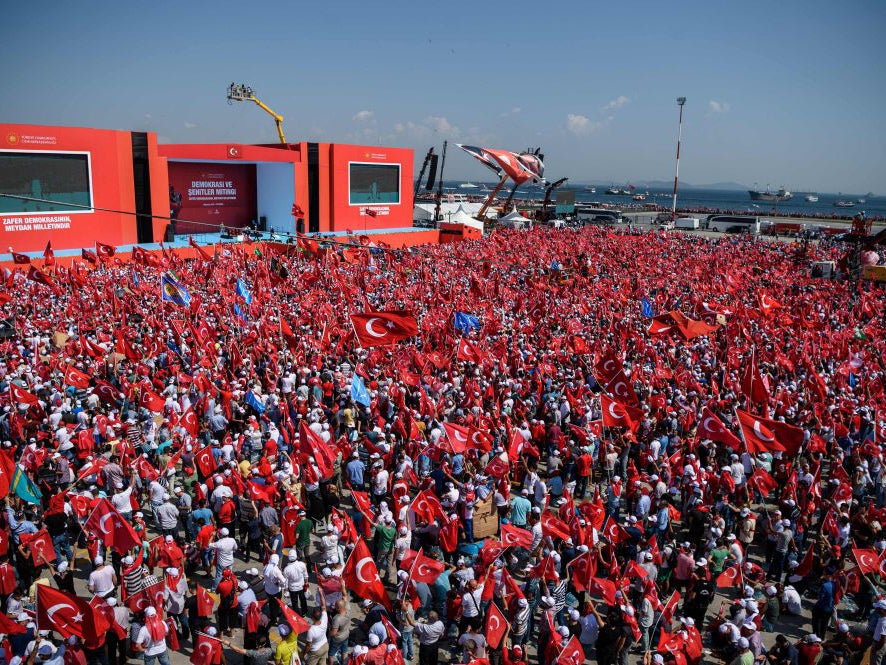 Demonstrators wave Turkish national flags as they stand in front of giant screens on August 7, 2016 in Istanbul during a rally against failed military coup on July 15