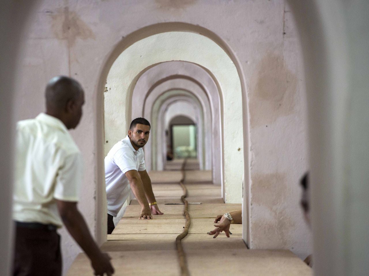Workers help Cuban cigar roller Jose "Cueto" Castelar, not pictured, hand roll a 90-meter cigar in Havana