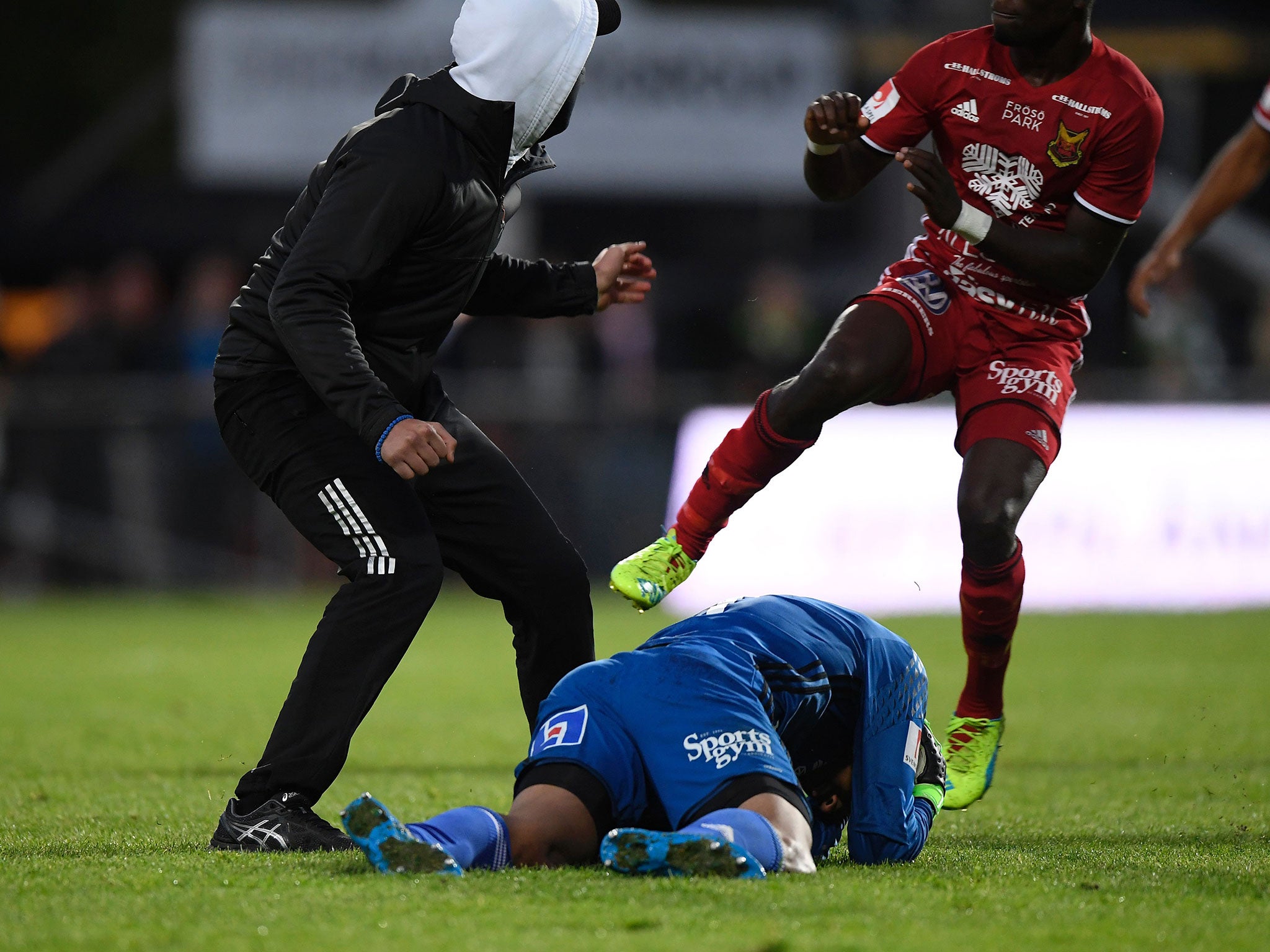 Ostersund's goalkeeper Aly Keita (R) remains on the ground after a masked spectator (L) attacked him during a football match between Jonkoping Sodra and Ostersund