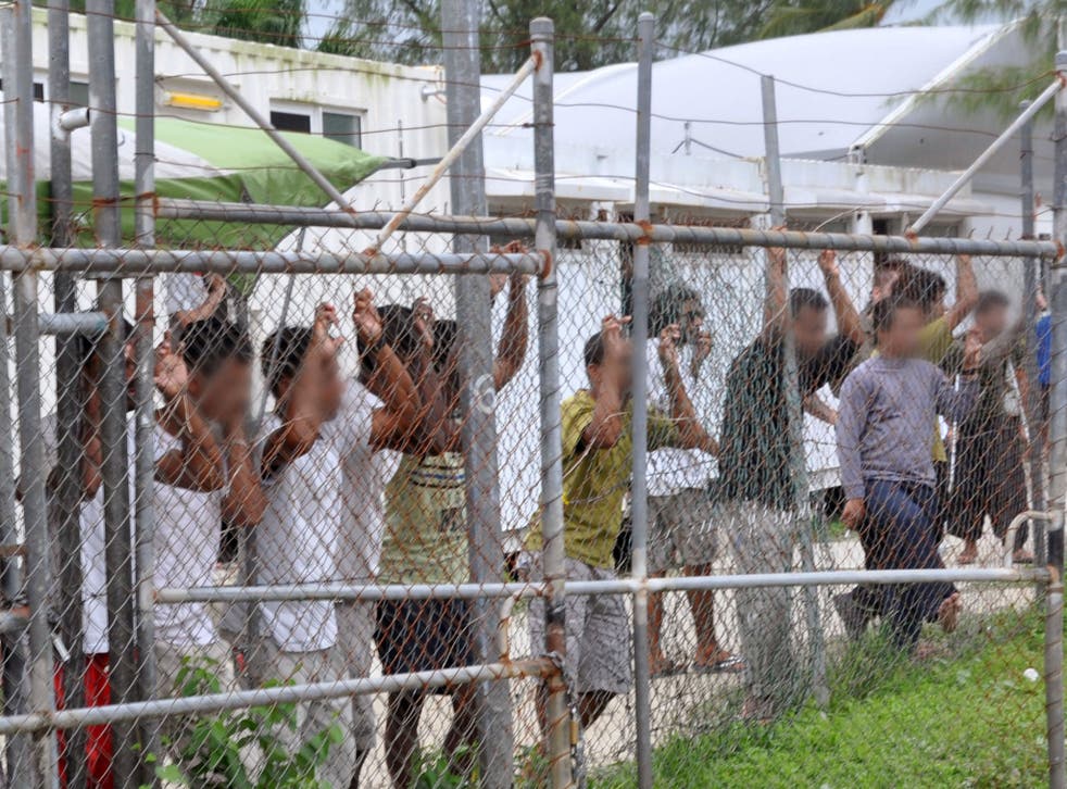 Asylum seekers look at the media from behind a fence at the Manus Island detention centre, Papua New Guinea in this picture taken March 21, 2014.