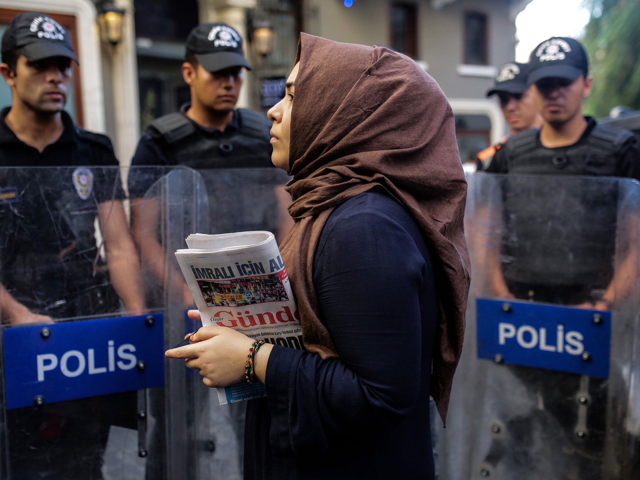 A woman holds a 'Ozgur Gundem' newspaper in front of a police barricade on August 16, 2016 in Istanbul.