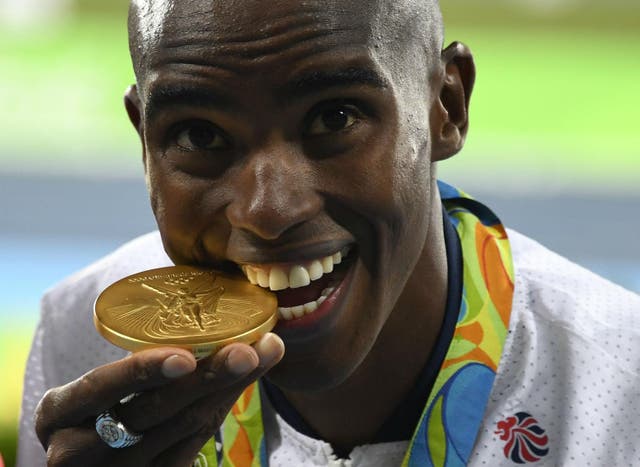 Mo Farah bites into his gold medal on the podium of the Men’s 10,000m