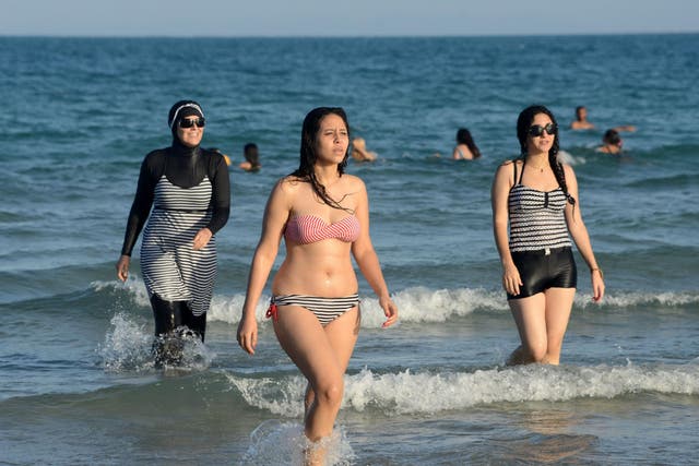 Tunisian women, one (L) wearing a "burkini", a full-body swimsuit designed for Muslim women, walk in the water on August 16, 2016 at Ghar El Melh beach near Bizerte, north-east of the capital Tunis.