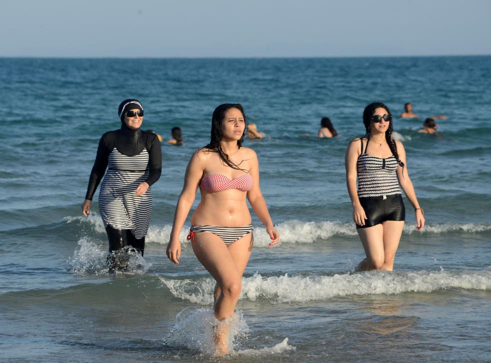 Tunisian women, one (L) wearing a "burkini", a full-body swimsuit designed for Muslim women, walk in the water on August 16, 2016 at Ghar El Melh beach near Bizerte, north-east of the capital Tunis.