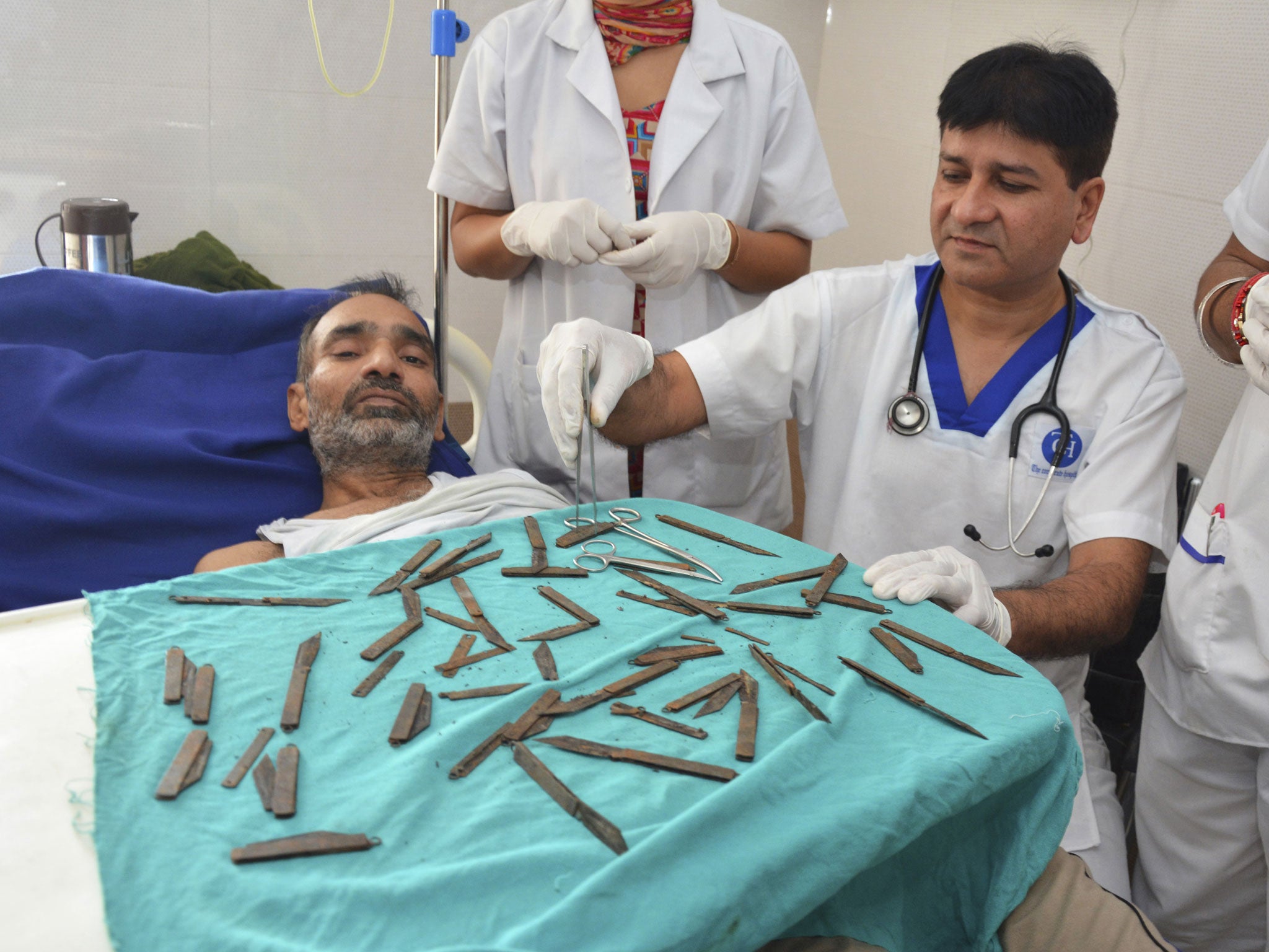 Jatinder Malhotra, right, displays the 40 knives that were surgically removed from the stomach of the police constable, as he recuperates in a hospital in Amritsar, India