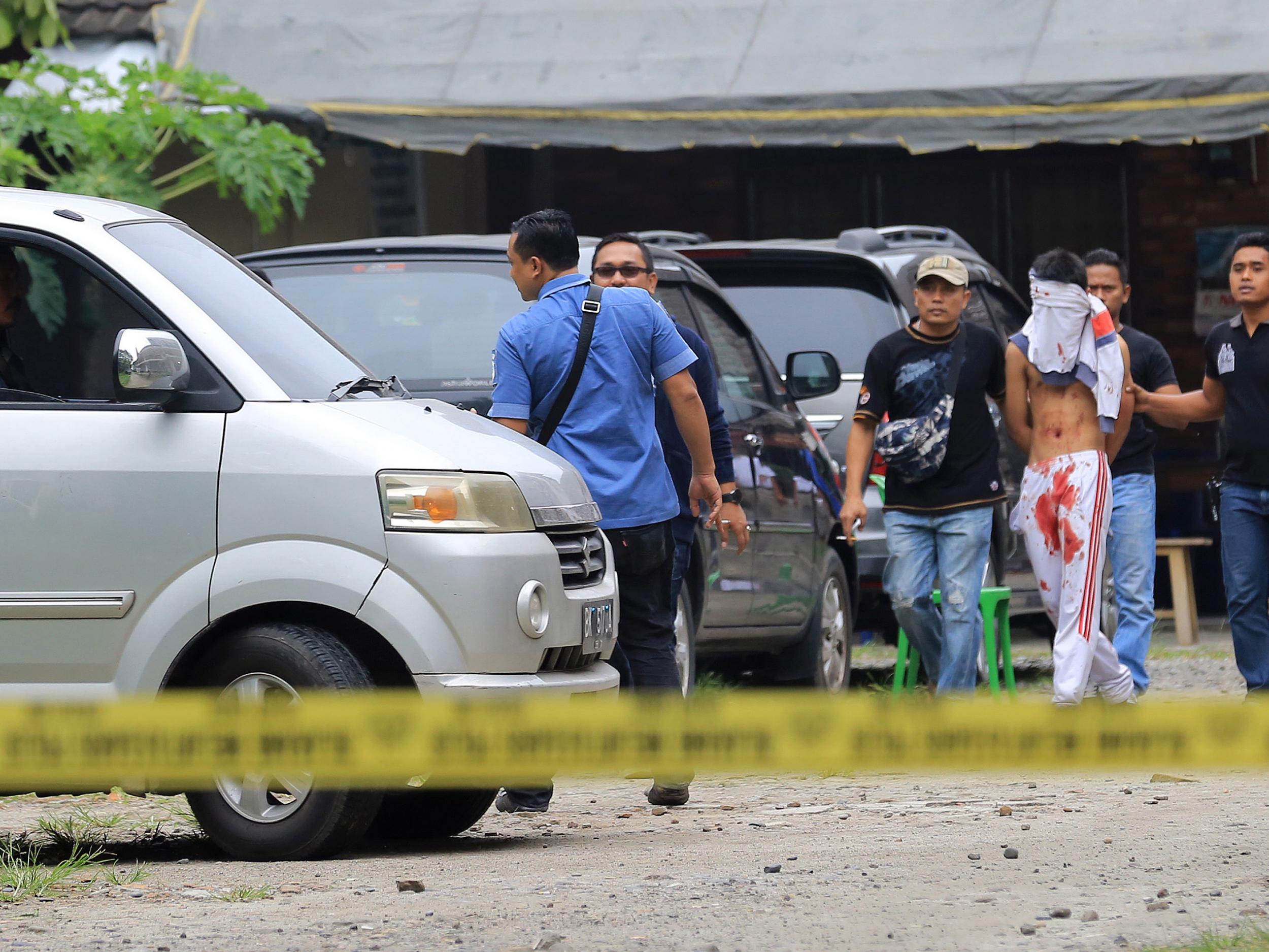 Indonesian policemen guard a blindfolded suspect who attacked a priest in Medan