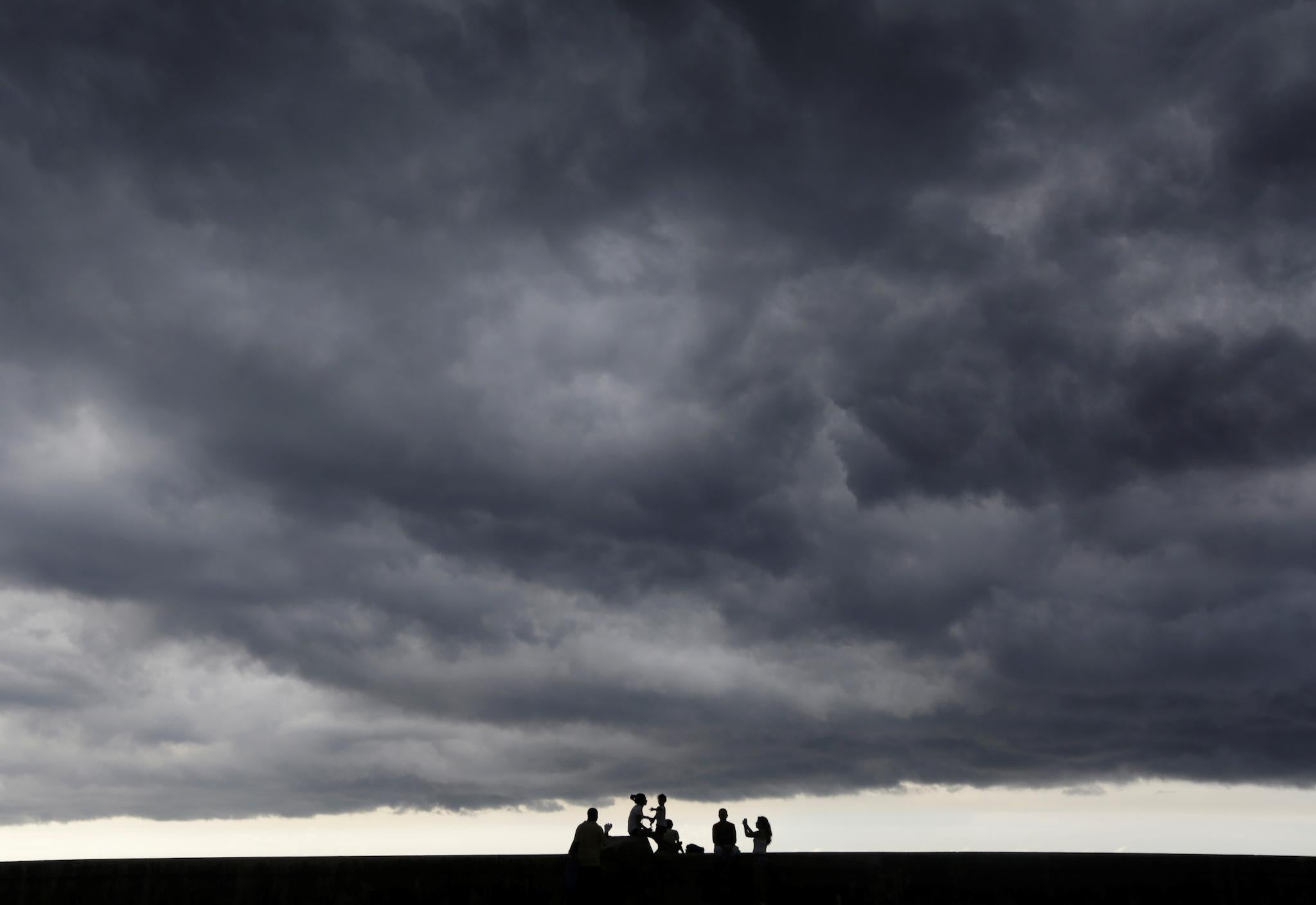 Storm clouds are seen in the sky as people sit on Havana's seafront boulevard El Malecon, Cuba
