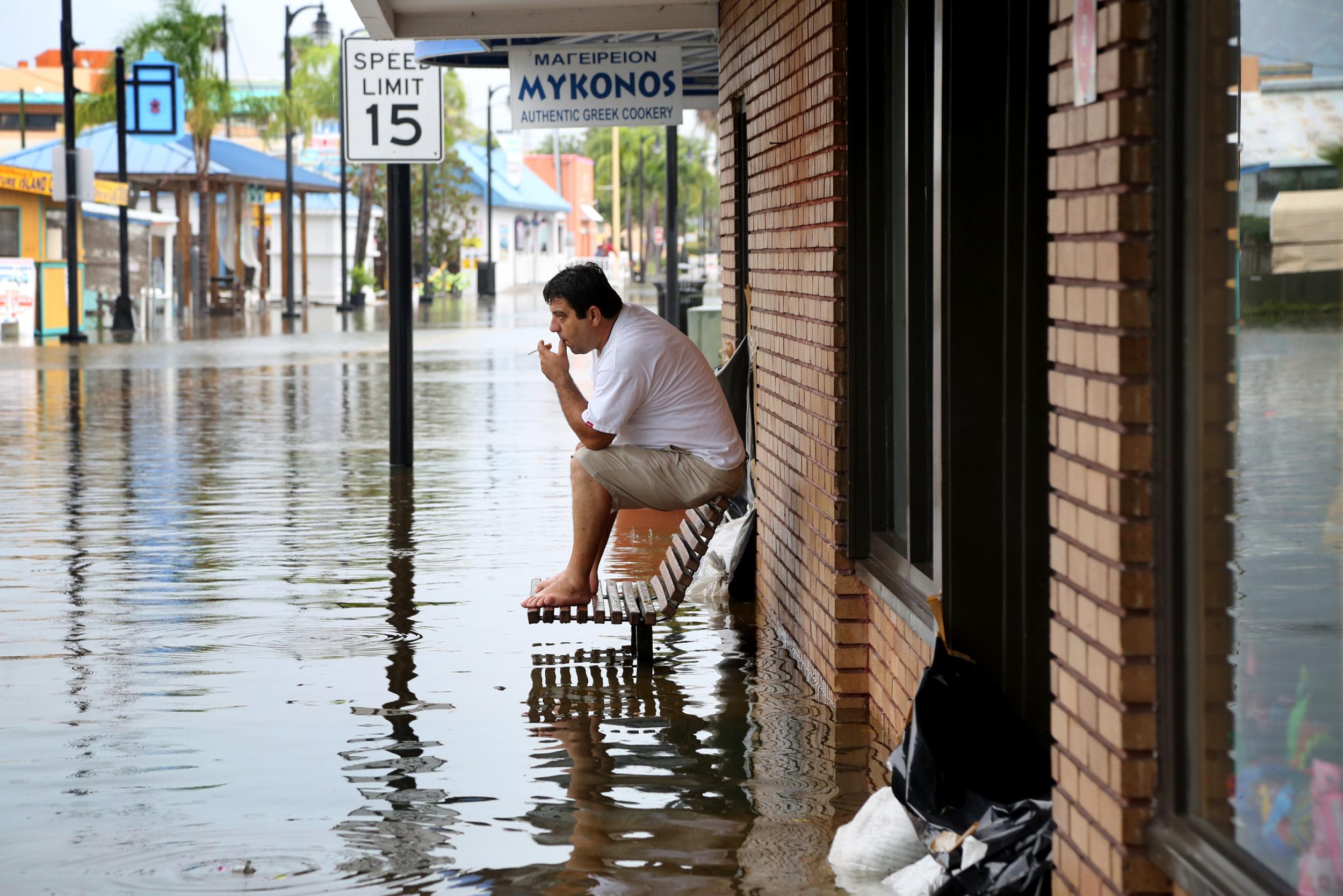 Pedro Muacaj rests on higher ground in front of a gift shop along a flooded section of Dodecanese Boulevard in Tarpon Springs, Florida