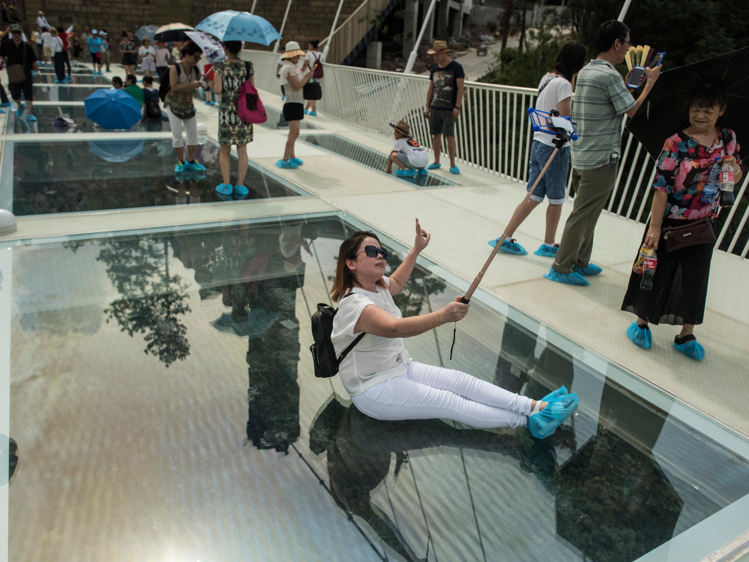 A tourist takes a photograph on the world's highest and longest glass-bottomed bridge