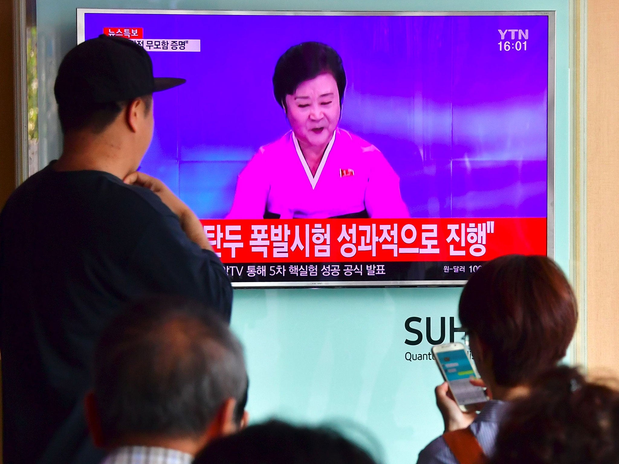 People watch a television news broadcast showing a North Korean anchor announcing the country's latest nuclear test, at a railway station in Seoul on September 9, 2016.