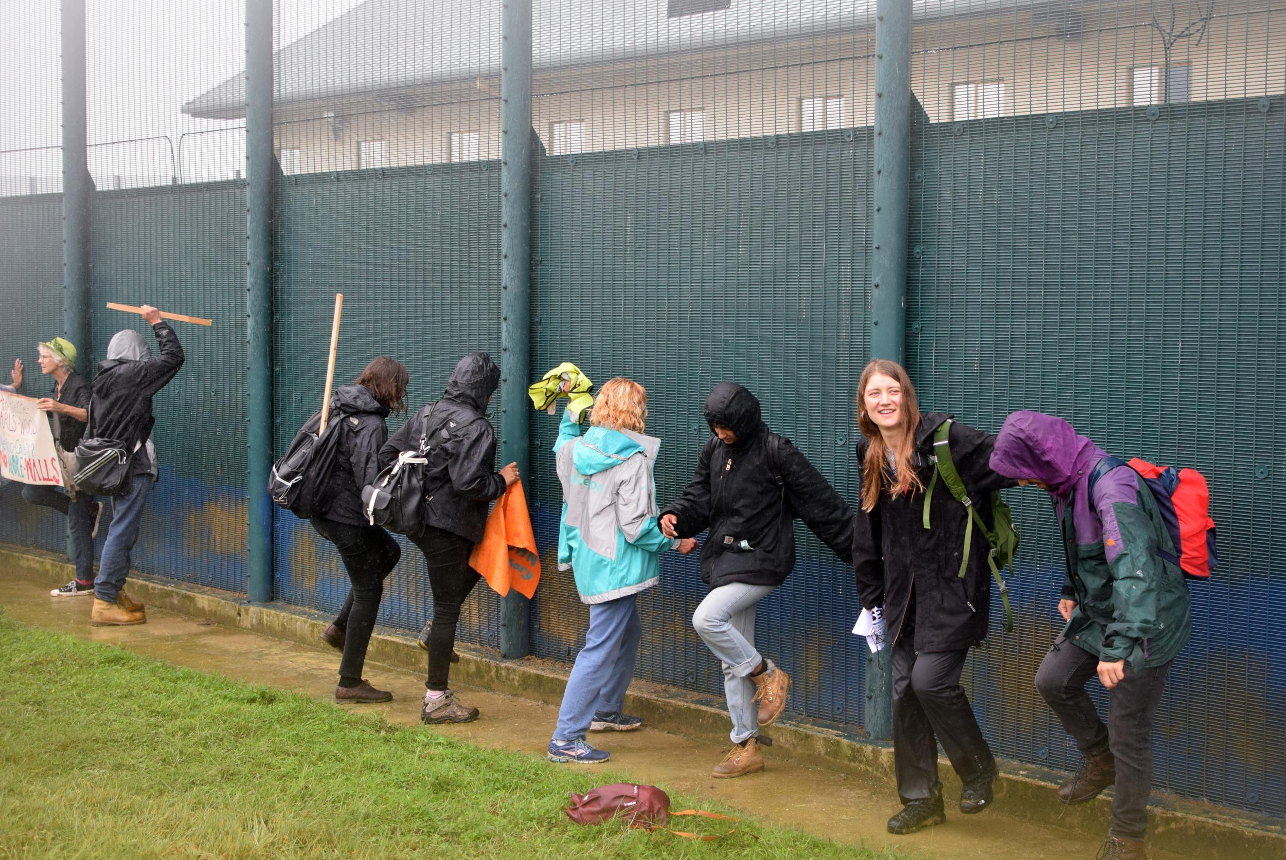 Protesters angrily kick and punch the metal perimeter fence surrounding the detention centre