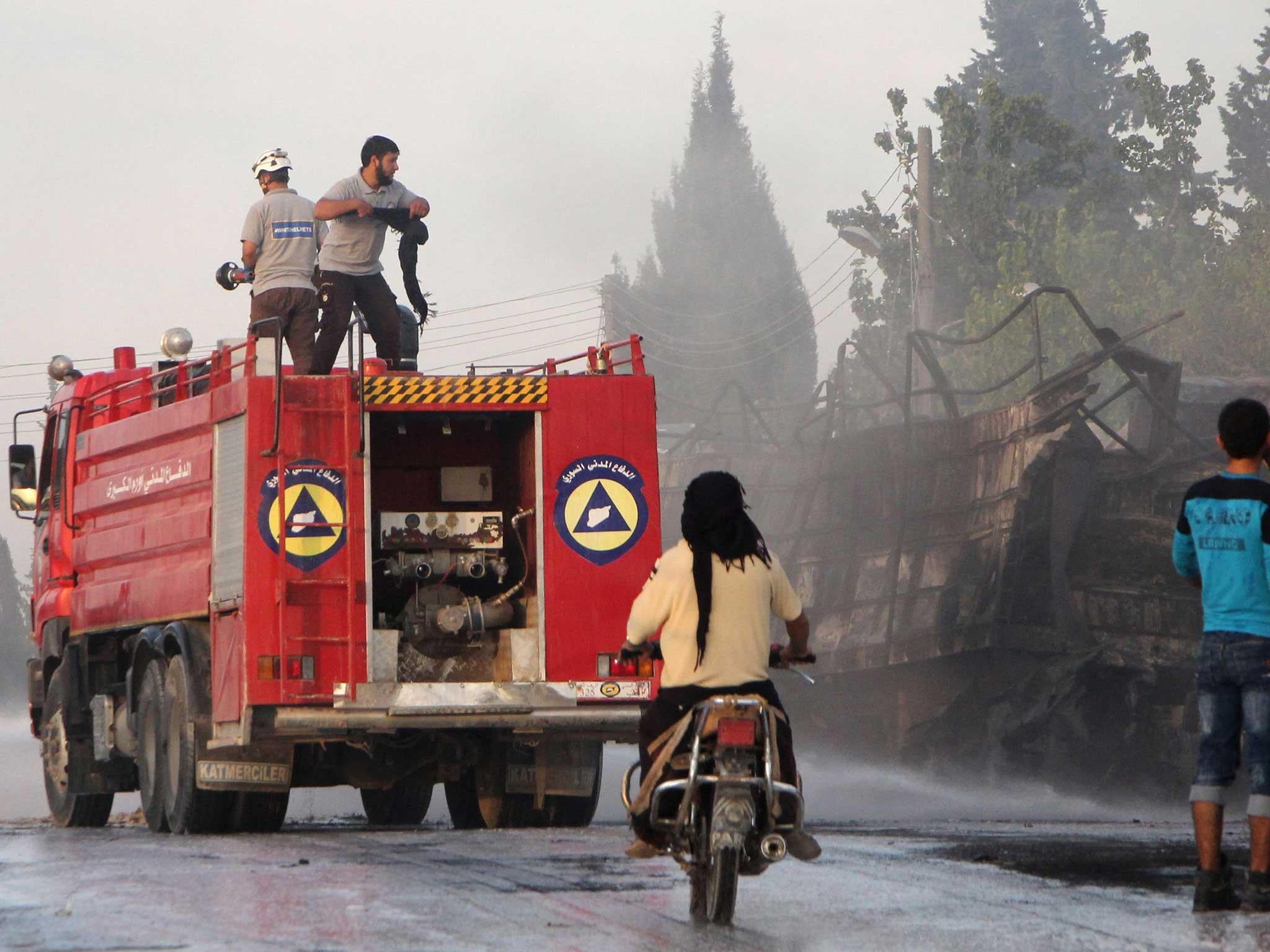 Members of the Syrian Civil Defence extinguish burning trucks carrying aid on the side of the road in the town of Orum al-Kubra on the western outskirts of the northern Syrian city of Aleppo