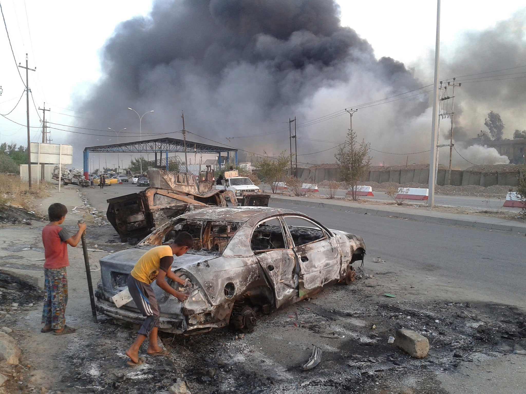 Civilian children stand next to a burnt vehicle during clashes between Iraqi security forces and Isis in Mosul, Iraq
