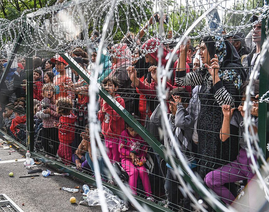 Refugees stand behind a fence at the Hungarian border with Serbia near the town of Horgos