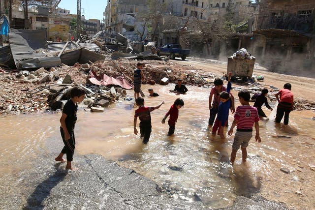 Children play in water from a burst pipe in the rubble of Aleppo