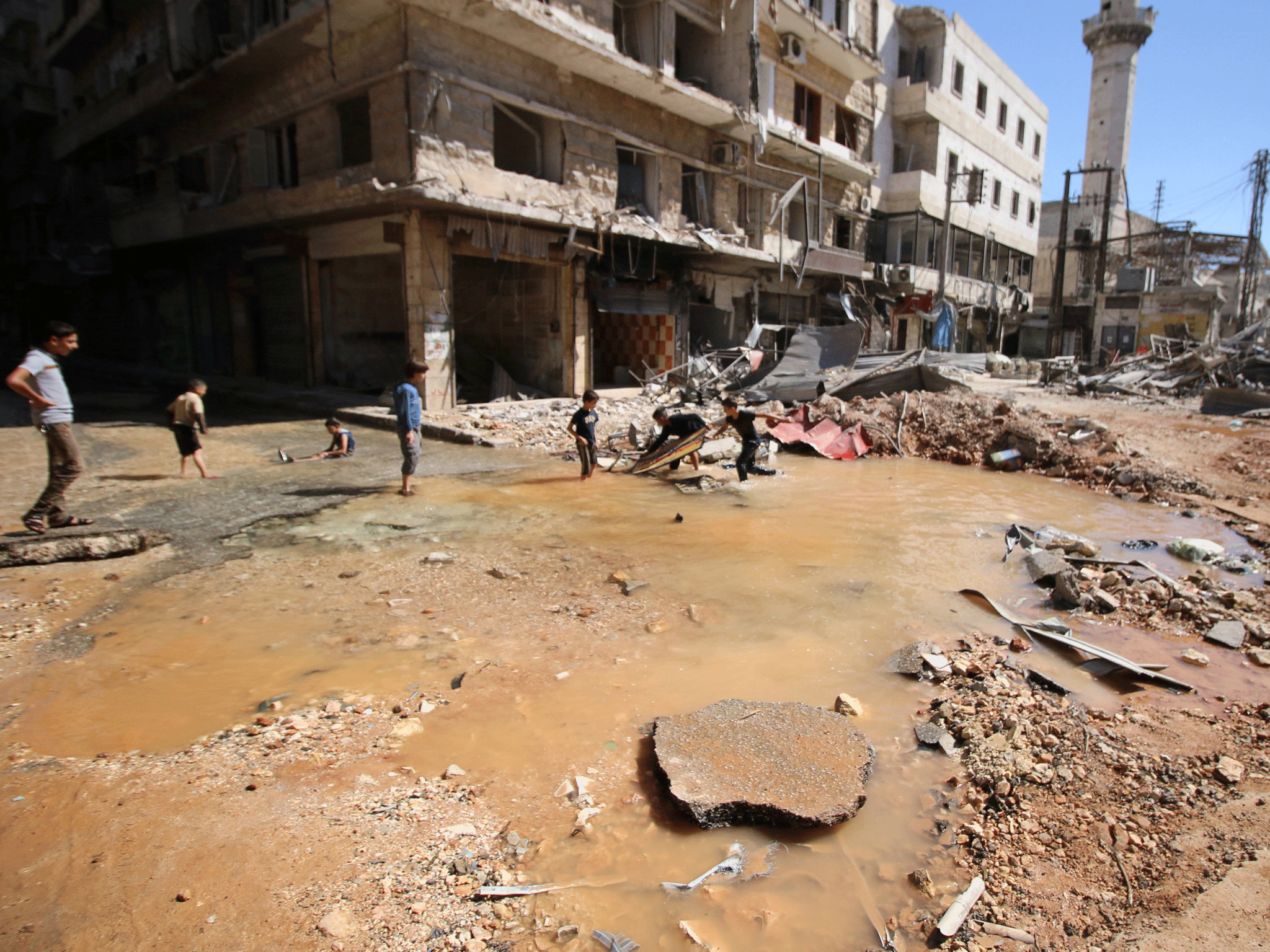 Children play with water from a burst water pipe at a site hit yesterday by an air strike in Aleppo's rebel-controlled al-Mashad neighbourhood