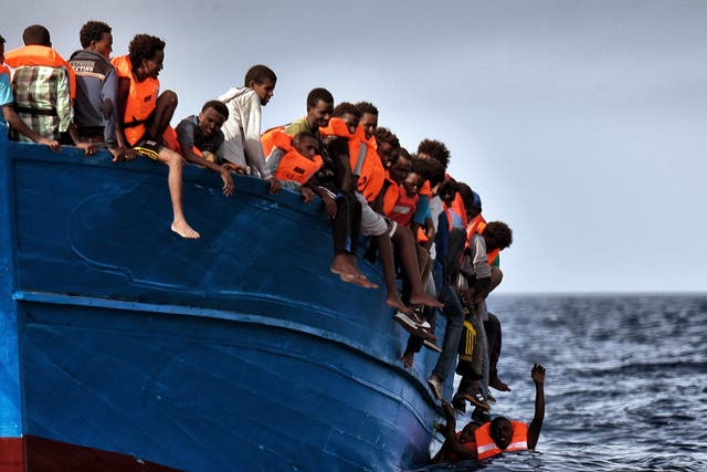 Migrants hang from a boat as they wait to be rescued yesterday 20 miles north of Libya
