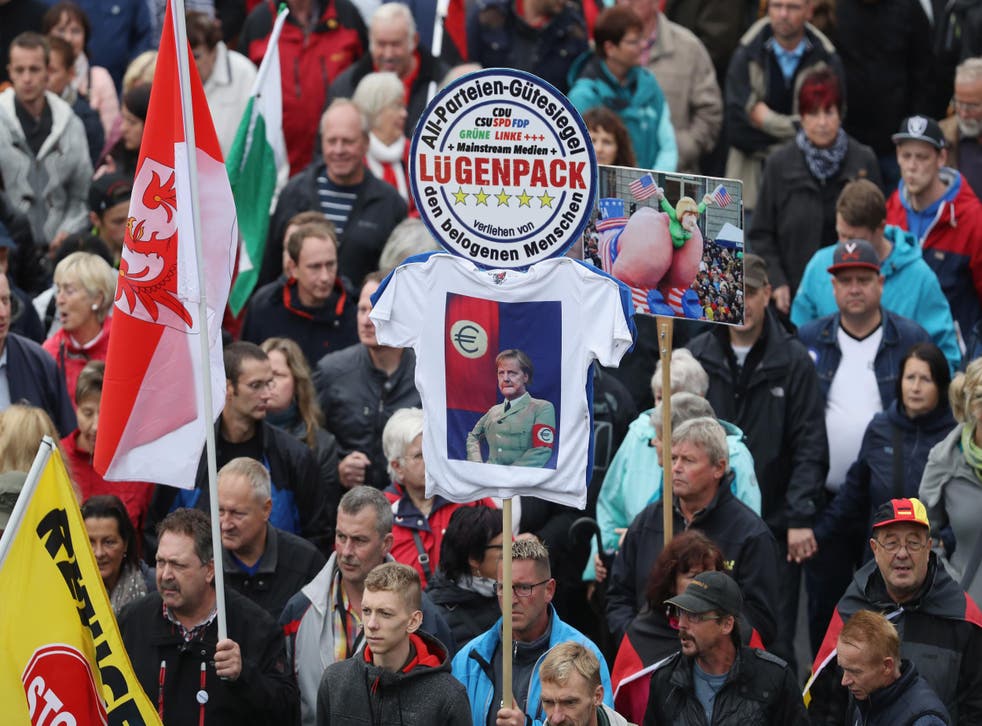 Pegida supporters, including one holding a sign that shows German Chancellor Angela Merkel dressed in a Nazi uniform