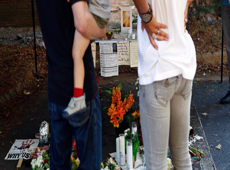 Adam and Tennille Fadel, hold their 21-month old child Alai, as they look at flowers and notes left by concerned community members at a small memorial at the scene of the death of Keith Scott September 23, 2016 in Charlotte, North Carolina. Scott, 43, was shot and killed by police officers at an apartment complex near UNC Charlotte, sparking protests.
