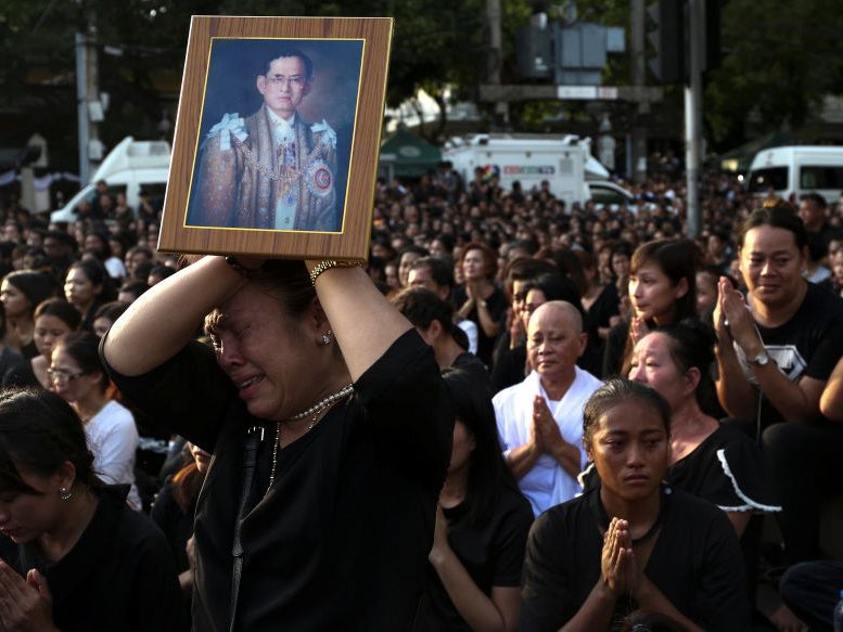 A man holds up a picture of the late King, as thousands line the streets during the procession of Thai King Bhumibol Adulyadej's body to his palace in Bangkok on October 14, 2016