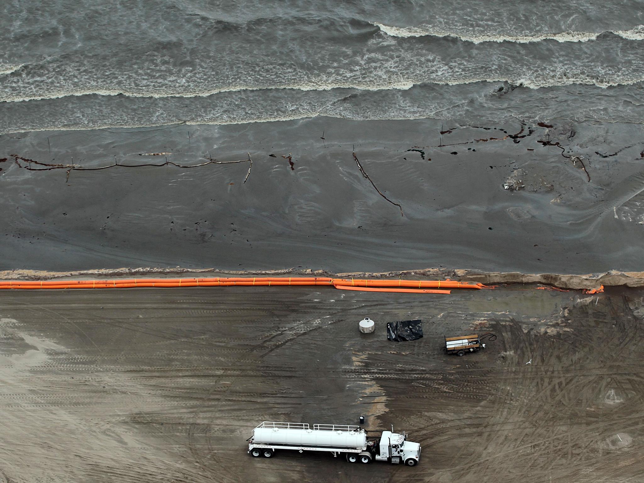 Oily absorbent material and containment booms are placed on the beach in efforts to clean up the oil spill