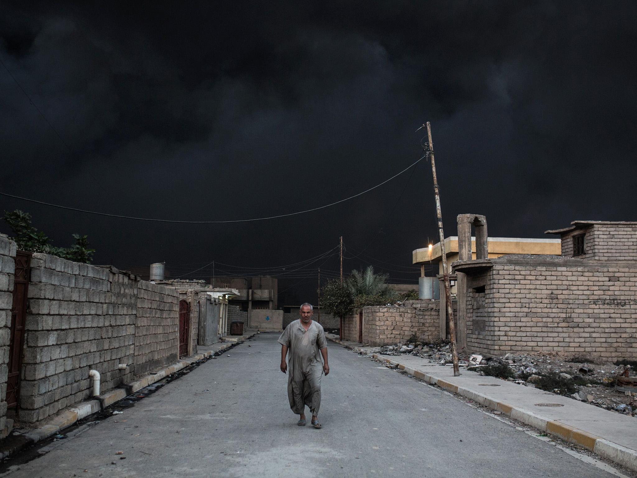 An Iraqi man walks on a street covered with smoke after an oil fire was set ablaze in the Qayyarah area, south of Mosul