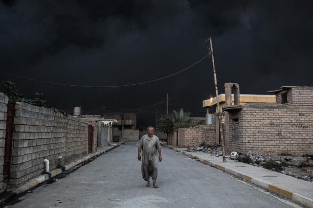 An Iraqi man walks on a street covered with smoke after an oil fire was set ablaze in the Qayyarah area, south of Mosul
