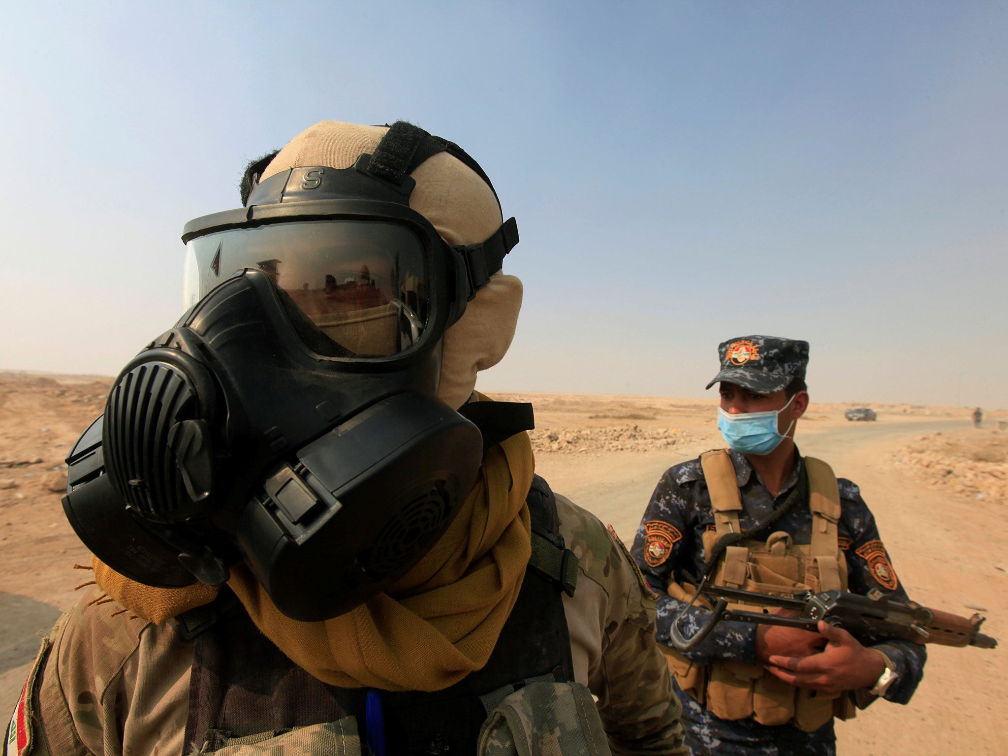 Iraqi forces wear protective masks to protect themselves from sulphur fumes from a plant set on fire by retreating Isis fighters near Mosul, Iraq, 22 October 2016.