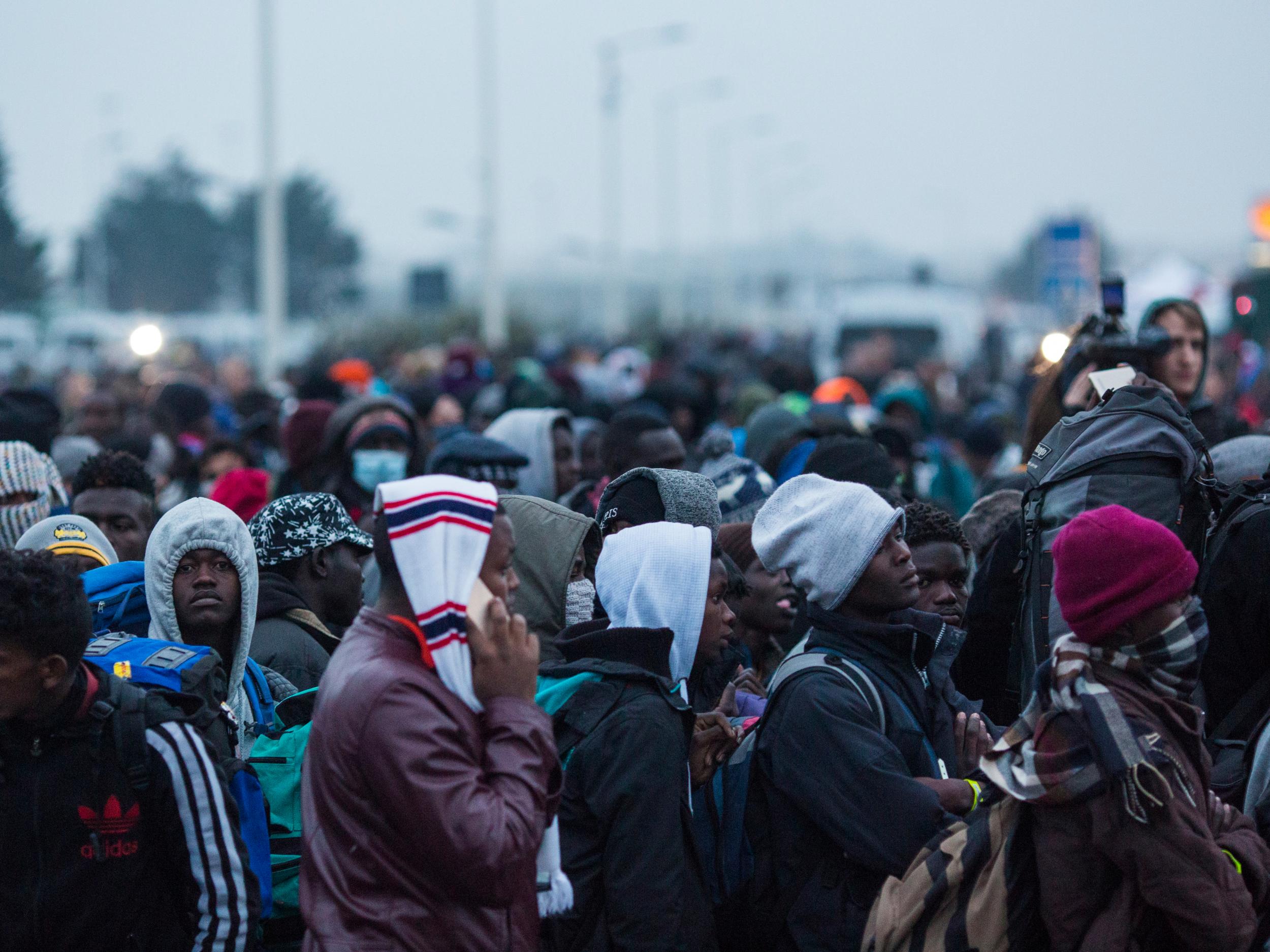 Migrants queue at a reception point outside the Jungle migrant camp