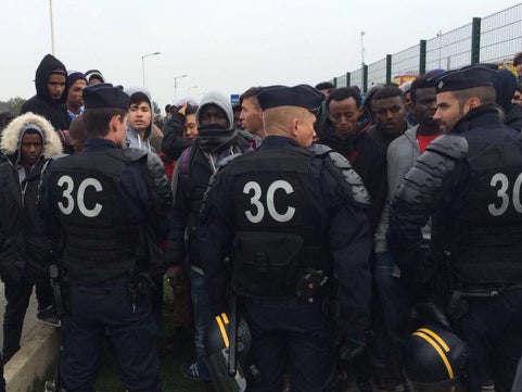 Refugees are surrounded by police as they begin to leave the Jungle camp