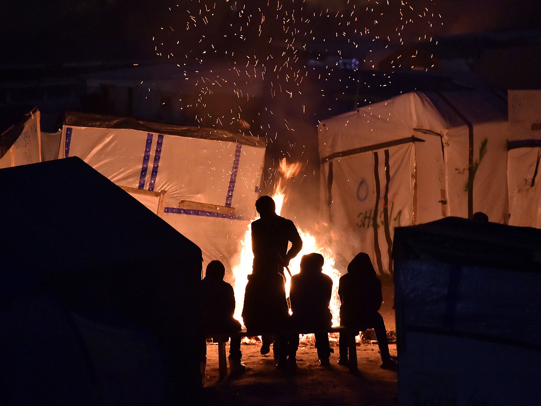 Migrants gather around a bonfire to warm up in the 'Jungle' migrant camp in Calais