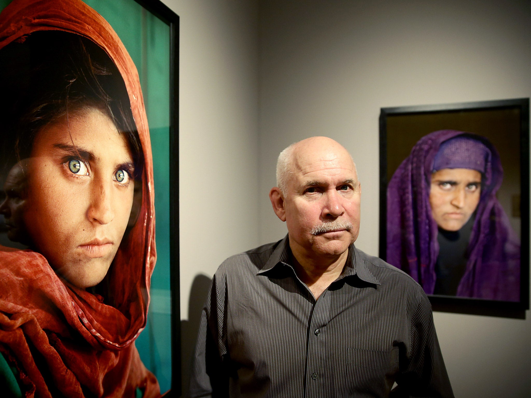 US photographer Steve McCurry poses next to his photos of the 'Afghan Girl' named Sharbat Gula at the opening of the 'Overwhelmed by Life' exhibition of his work