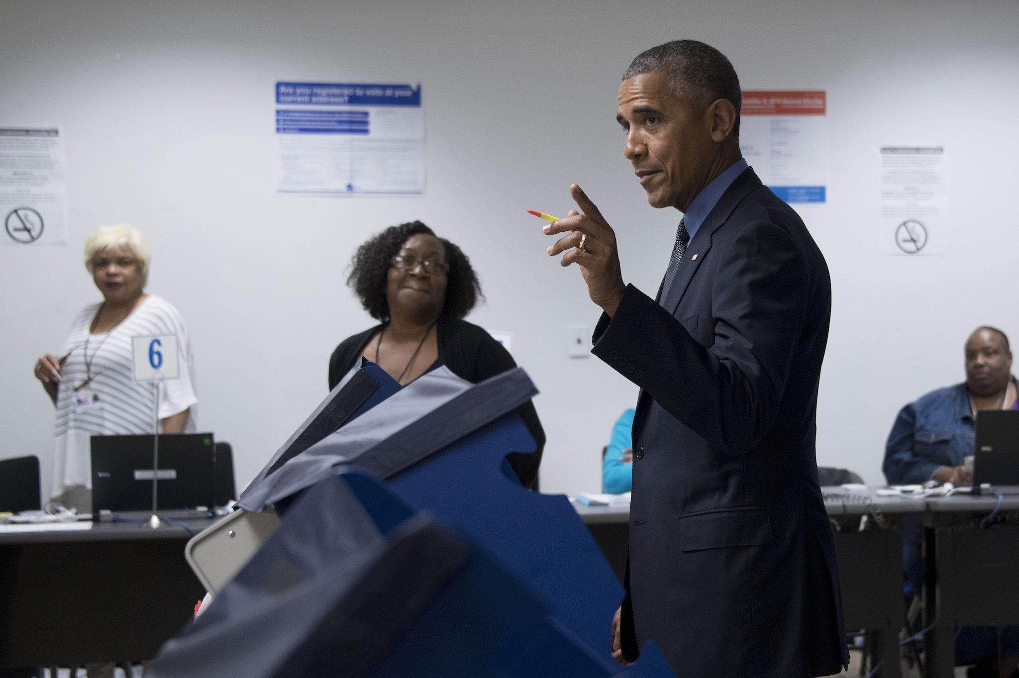 Poll workers look on as US President Barack Obama (C) gestures towards the press as he votes early at the Cook County Office Building in Chicago, Illinois, October 7, 2016