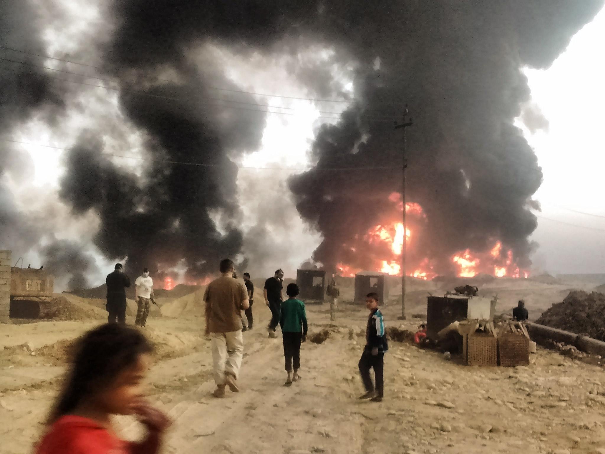 Children playing near the burning oil wells of Qayyarah