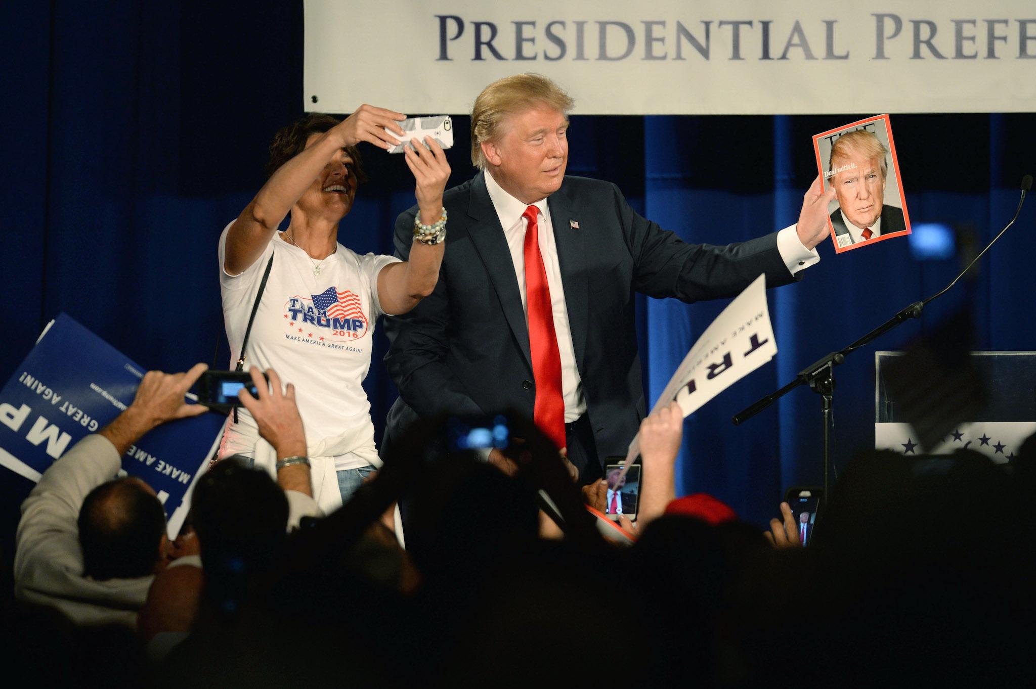 Republican presidential candidate Donald Trump holds a copy of TIME magazine with his likeness of the cover as a woman tries to take a selfie at the National Federation of Republican Assemblies (NFRA) Presidential Preference Convention at Rocketown on August 29, 2015 in Nashville, Tennessee