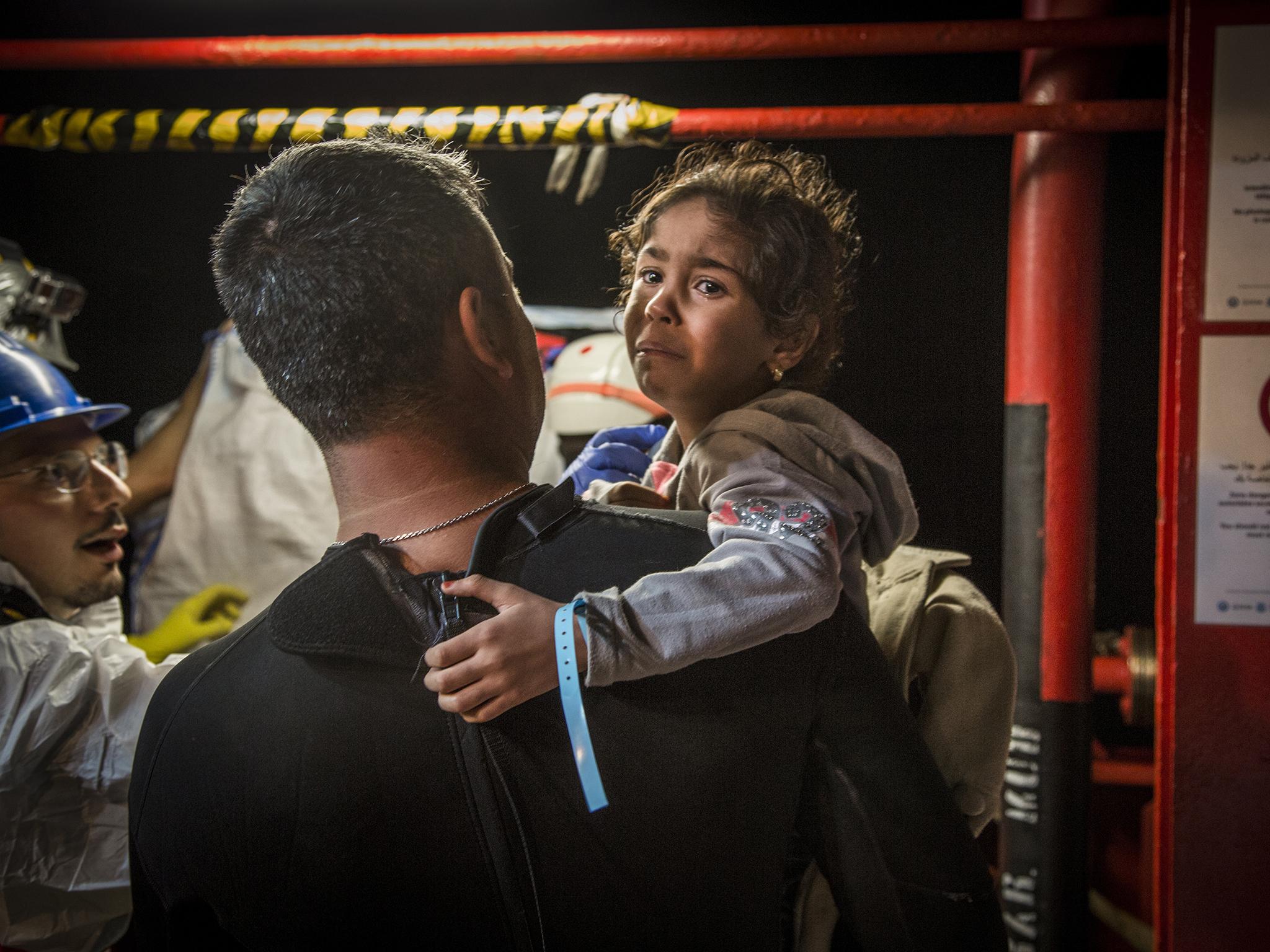 A Worker with the international charitable organisation Save the Children carries a young Syrian girl, brought aboard the Vos Hestia after being rescued from a migrant boat in the Mediterranean Sea