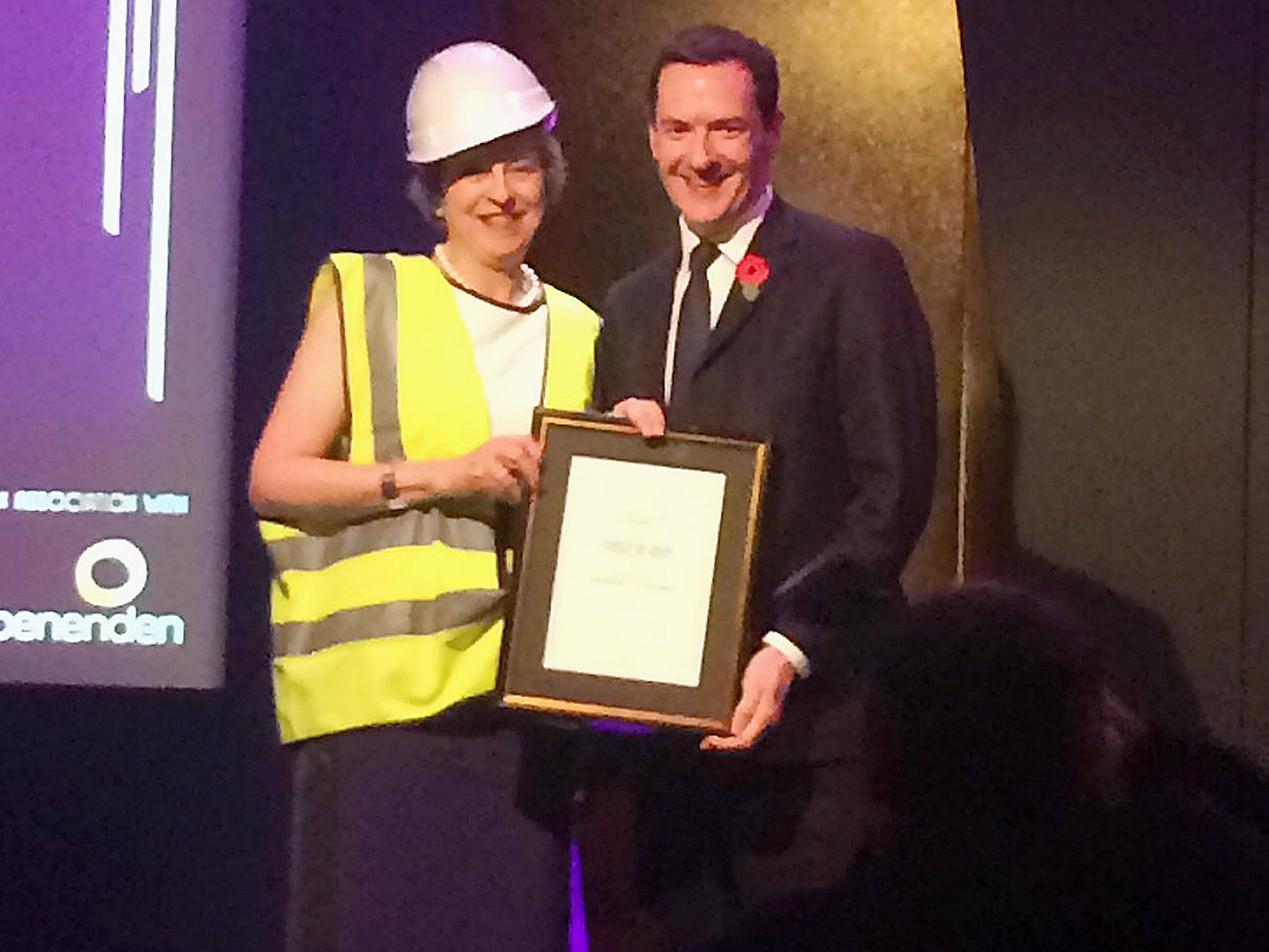 Prime Minister Theresa May who appeared to mock George Osborne by accepting an award from the former chancellor wearing a high-visibility jacket and hard hat