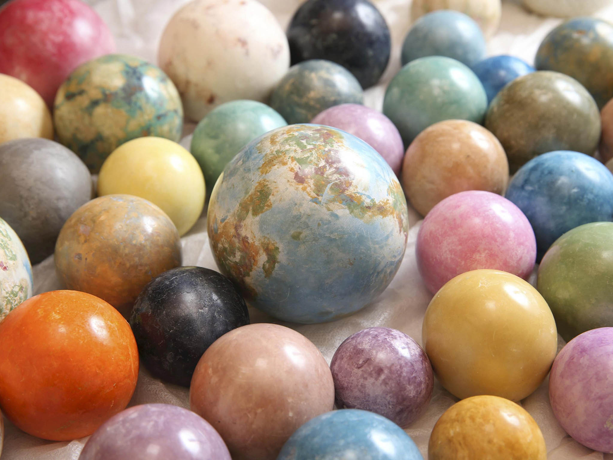 Colorful dorodango mudballs are displayed. The one in the middle is painted with several colors to look like the Earth