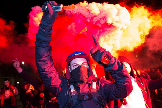 A masked protester holds up a flare on Whitehall