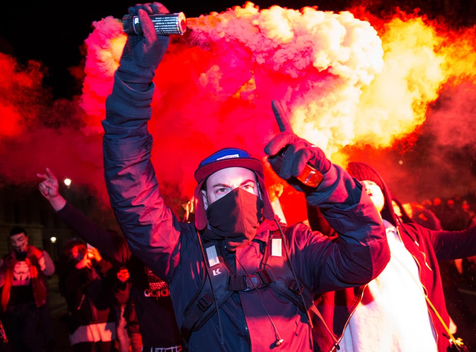 A masked protester holds up a flare on Whitehall
