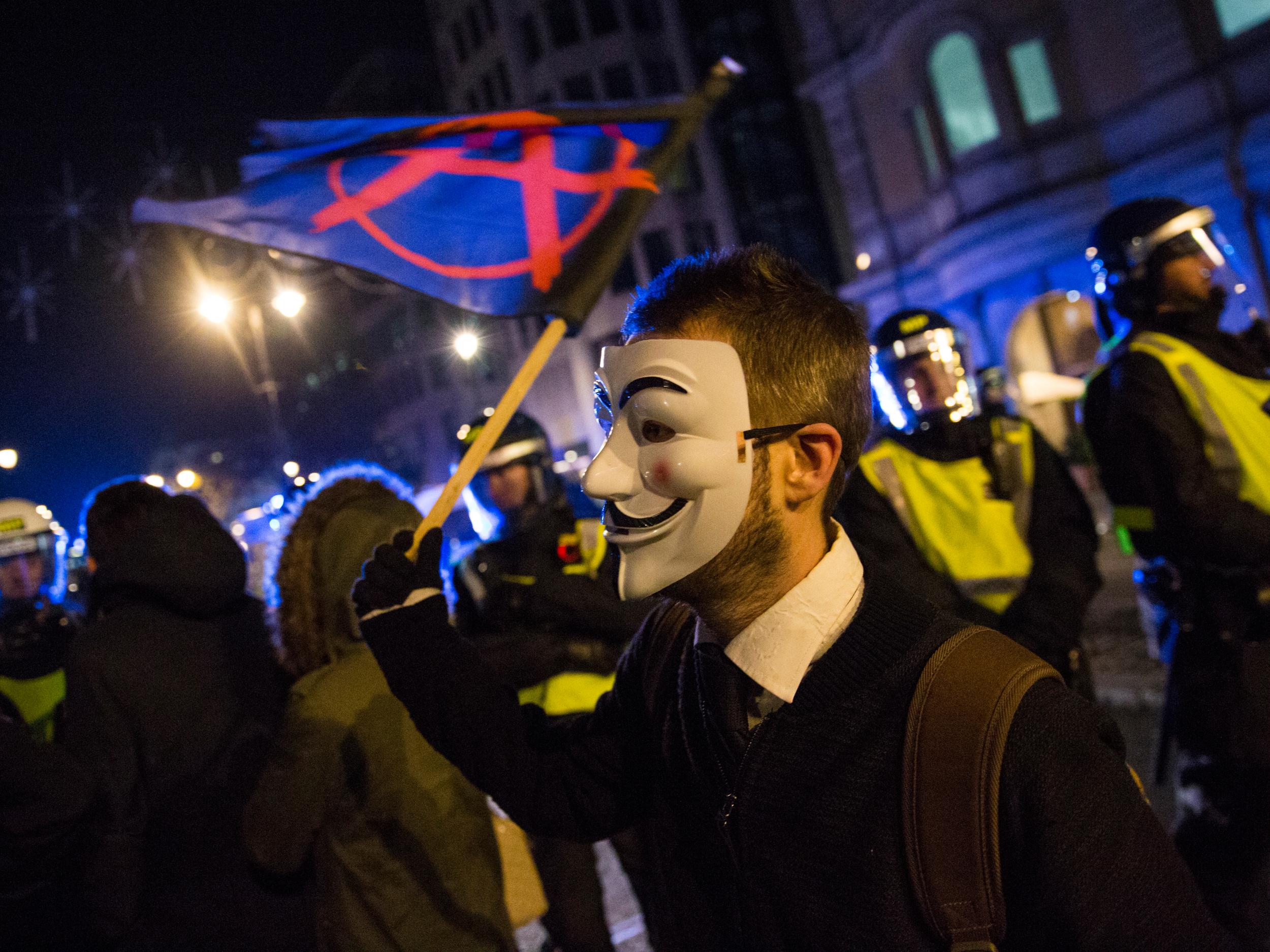A masked protester waves an 'Anarchy' flag in front of a line of police (Getty Images )