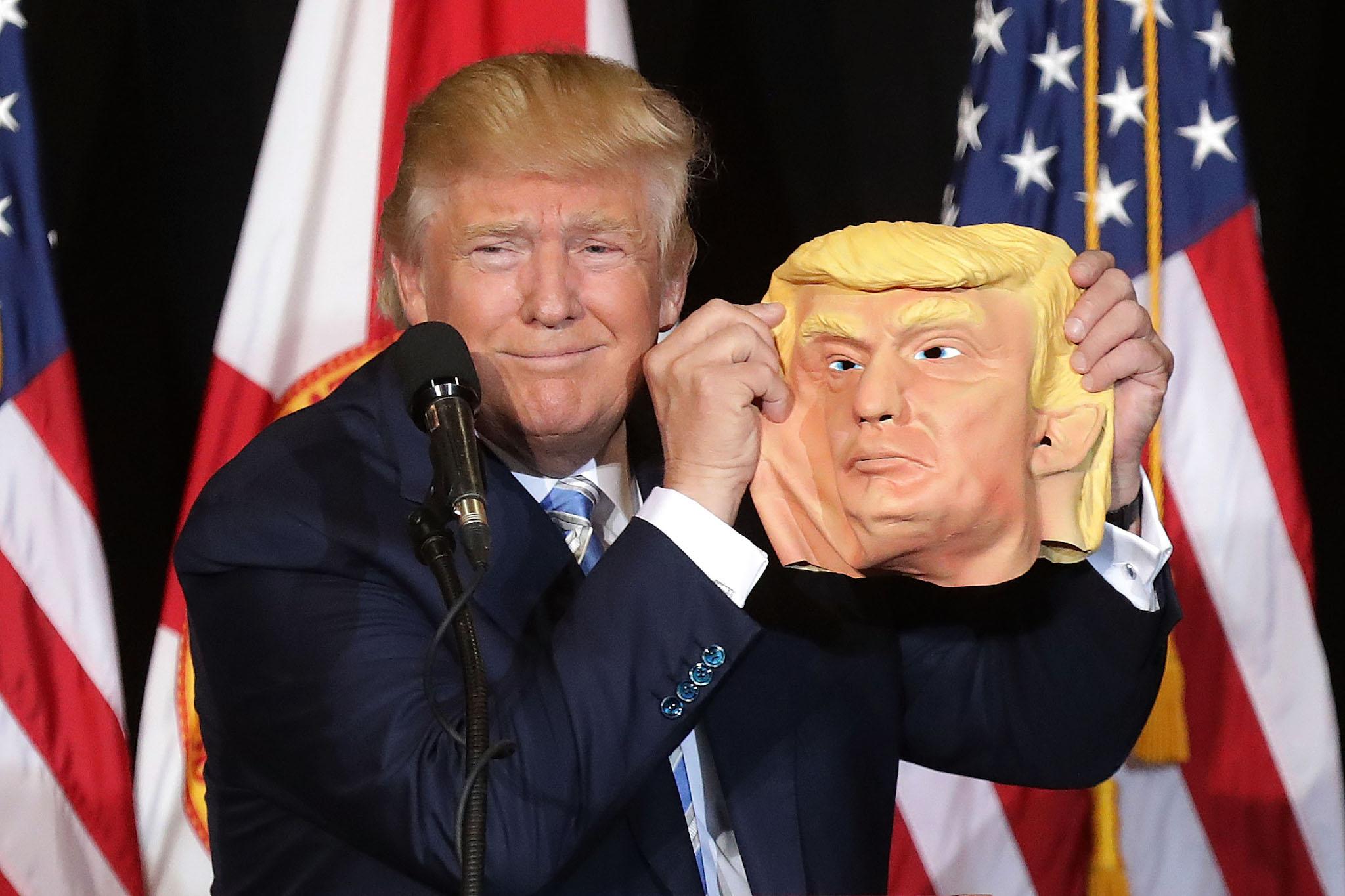 Republican presidential nominee Donald Trump holds up a rubber mask of himself during a campaign rally in the Robarts Arena at the Sarasota Fairgrounds November 7, 2016 in Sarasota, Florida