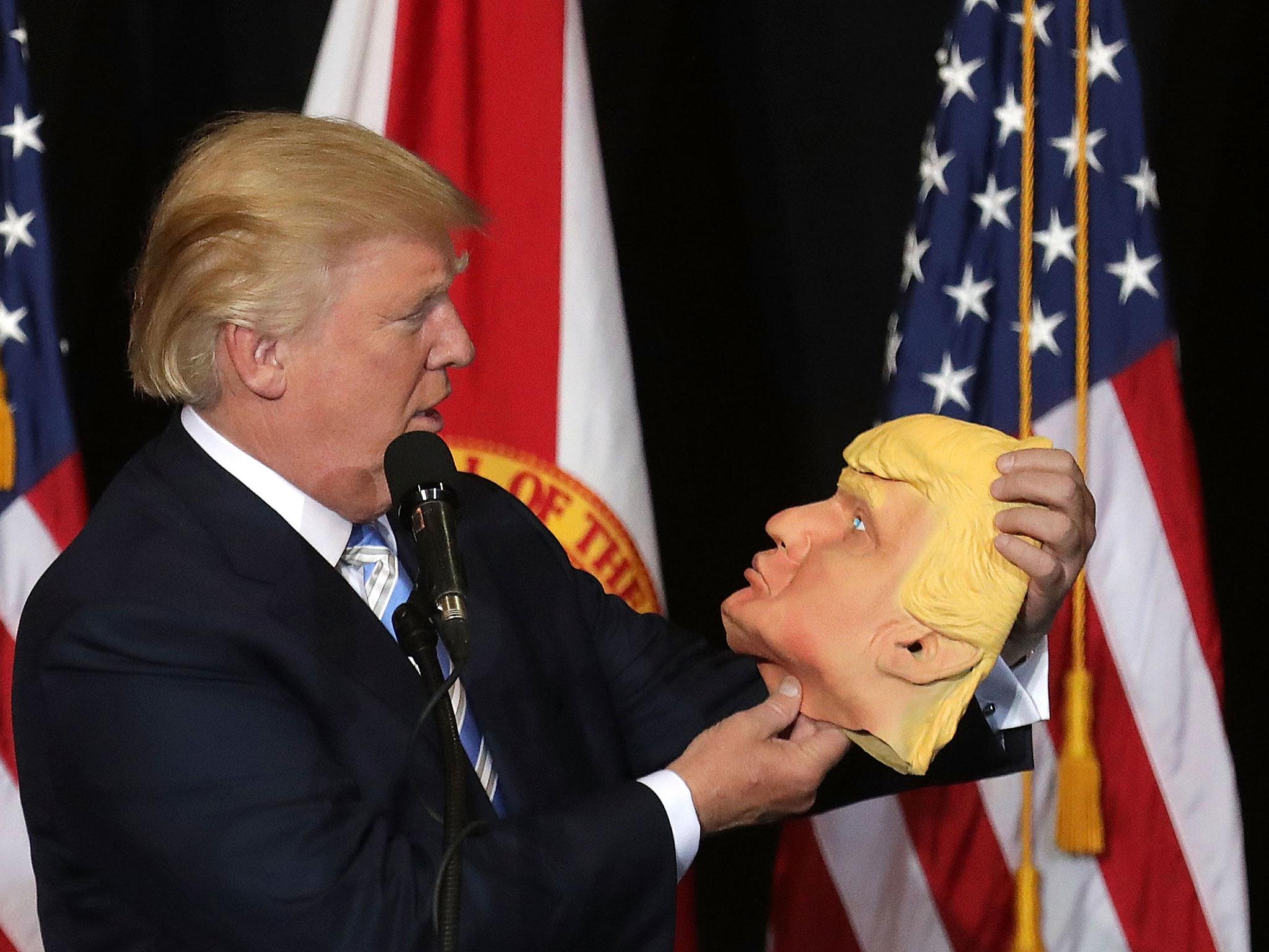 Republican presidential nominee Donald Trump holds up a rubber mask of himself during a campaign rally in the Robarts Arena at the Sarasota Fairgrounds 7 November, 2016 in Sarasota, Florida